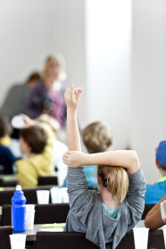 Ein junges Mädchen sitzt bei der Kinder-Uni am Tisch und meldet sich