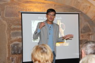 Heimatforscher Adrian Roßner hält seinen Vortrag vor den Besuchern. Im Hintergrund läuft seine Präsentation auf einer Leinwand.