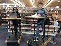 Zwei Menschen laufen in einer Bibliothek auf Laufbändern, während sie am Lernen sind.