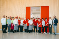 das 22-köpfige Team von Infraserv mit rot-weißer Firmenbekleidung vor einer Holzwand