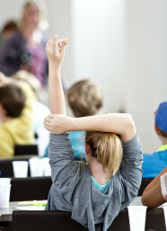 Ein junges Mädchen sitzt bei der Kinder-Uni am Tisch und meldet sich
