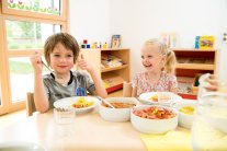 Junge und Mädchen sitzen am Esstisch und zeigen den Daumen hoch