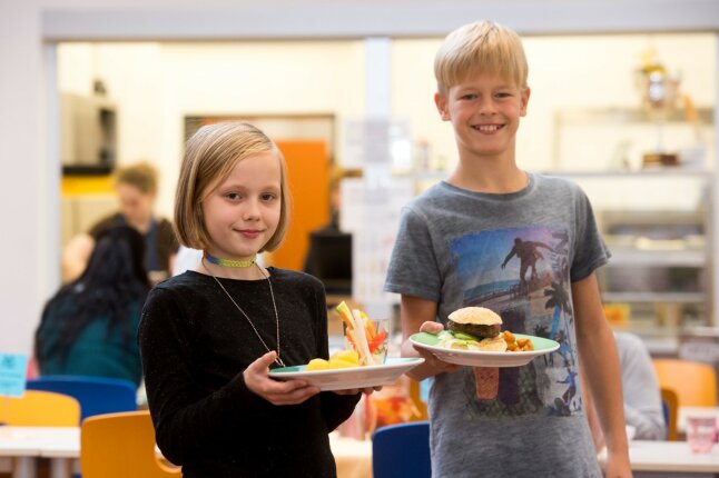 Ein Mädchen und ein Junge halten lächelnd einen Teller mit Essen in der Hand