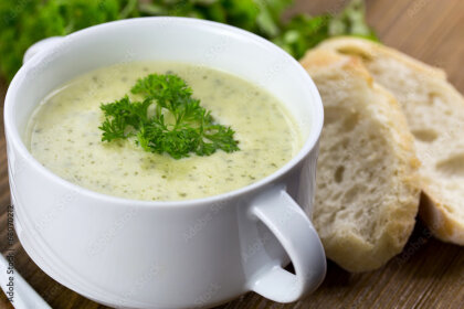 Eine Suppenschale gefüllt mit einer cremigen Kräutersuppe, Weißbrot als Beilage