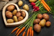 Kartoffeln in einer Herz-Form neben Karotten und Radieschen