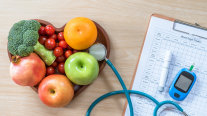 Herzförmige Schale mit Obst und Gemüse, die neben Fragebogen und Blutzuckermessgerät liegt