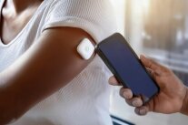Arm mit Blutzuckermess-Sensor, an den ein Handy zum Auslesen gehalten wird