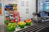 Obstschalen mit Äpfeln und Bananen stehen vor dem Süßigkeitenständer an der Kasse