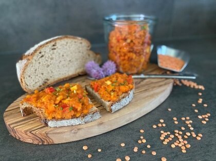 Brot mit orangefarbenem Linsenaufstrich, serviert auf einem Holzbrett