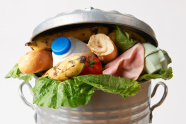 Foto  Das Foto zeigt eine Mülltonne. Sie quillt schon über. Das heißt sie ist zu voll mit Lebensmittel.