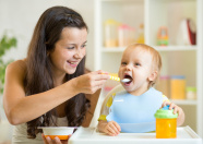 Frau füttert Kleinkind am Essenstisch.
